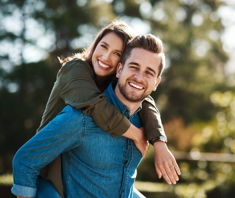 Happy couple smiling brightly after Ridge Augmentation treatment at Craft Dental, enjoying outdoor moment.